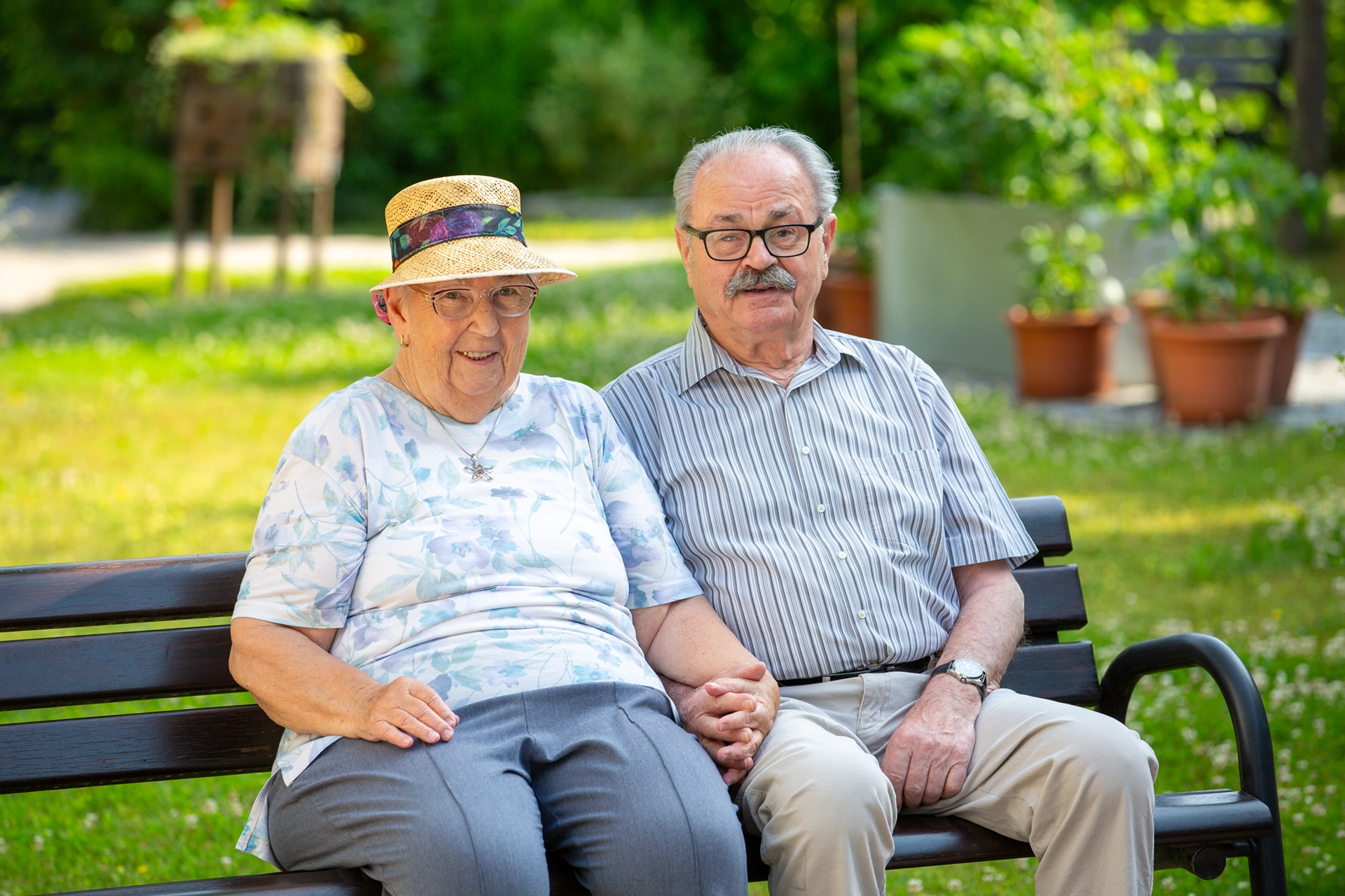 Seniorenpaar sitzt Hand in Hand im Garten eines Pflegeheims der Geraer Heimbetriebsgesellschaft und lächelt in die Kamera