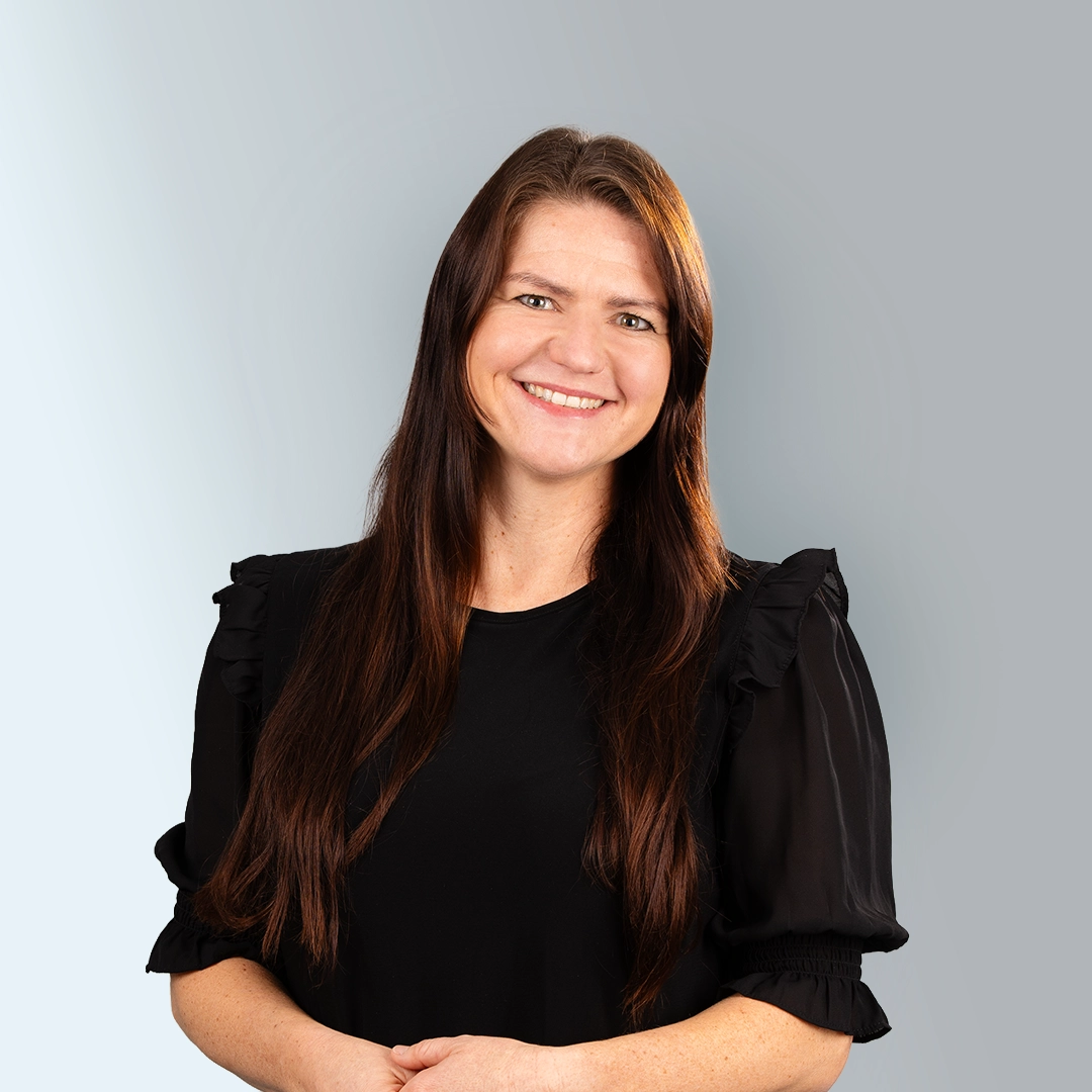 Porträt einer Mitarbeiterin der Geraer Heimbetriebsgesellschaft mbH mit langen braunen Haaren und freundlichem Lächeln vor neutralem Hintergrund