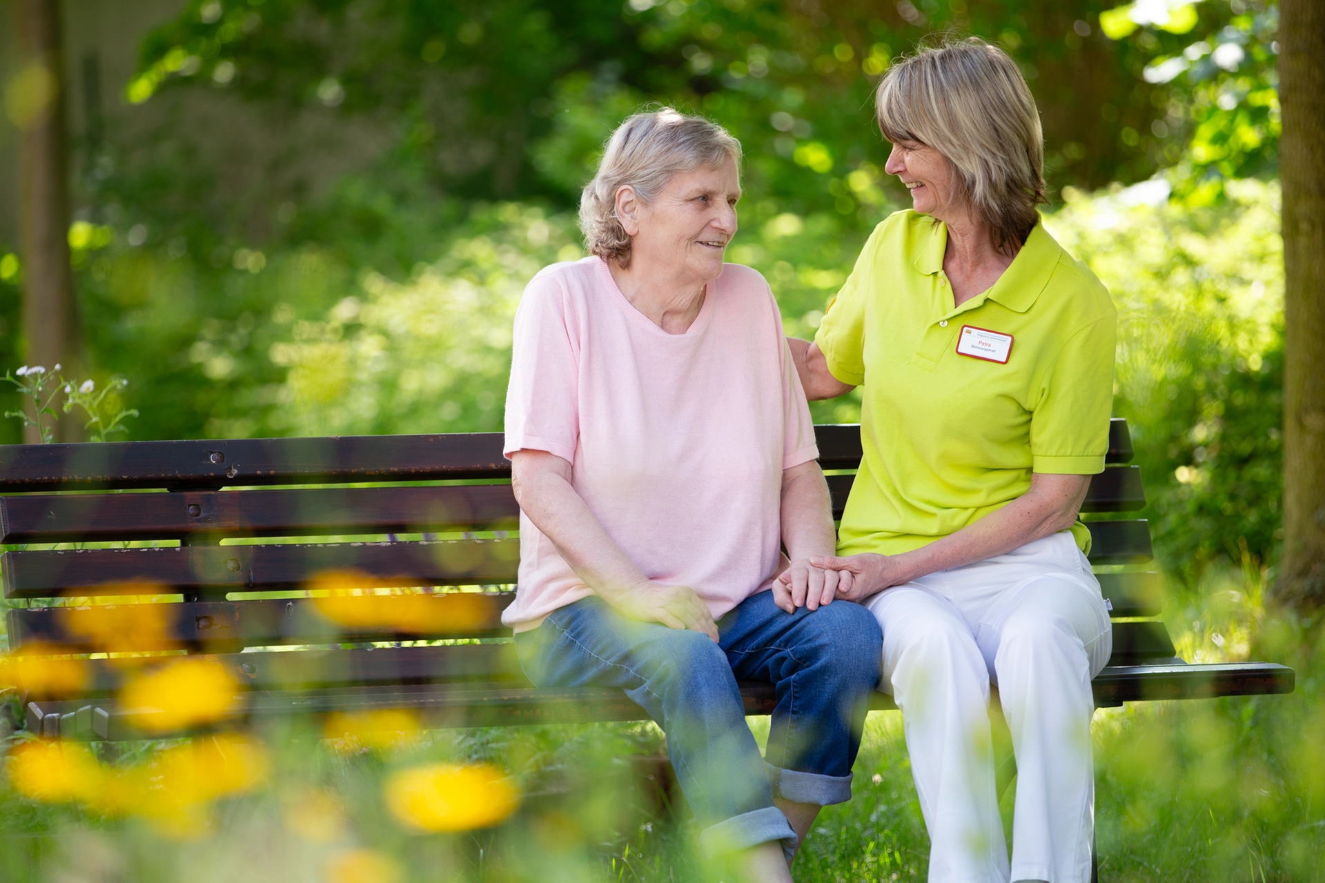 Pflegekraft sitzt mit einer Bewohnerin auf einer Bank im Garten des Pflegeheims Am Hofwiesenpark.