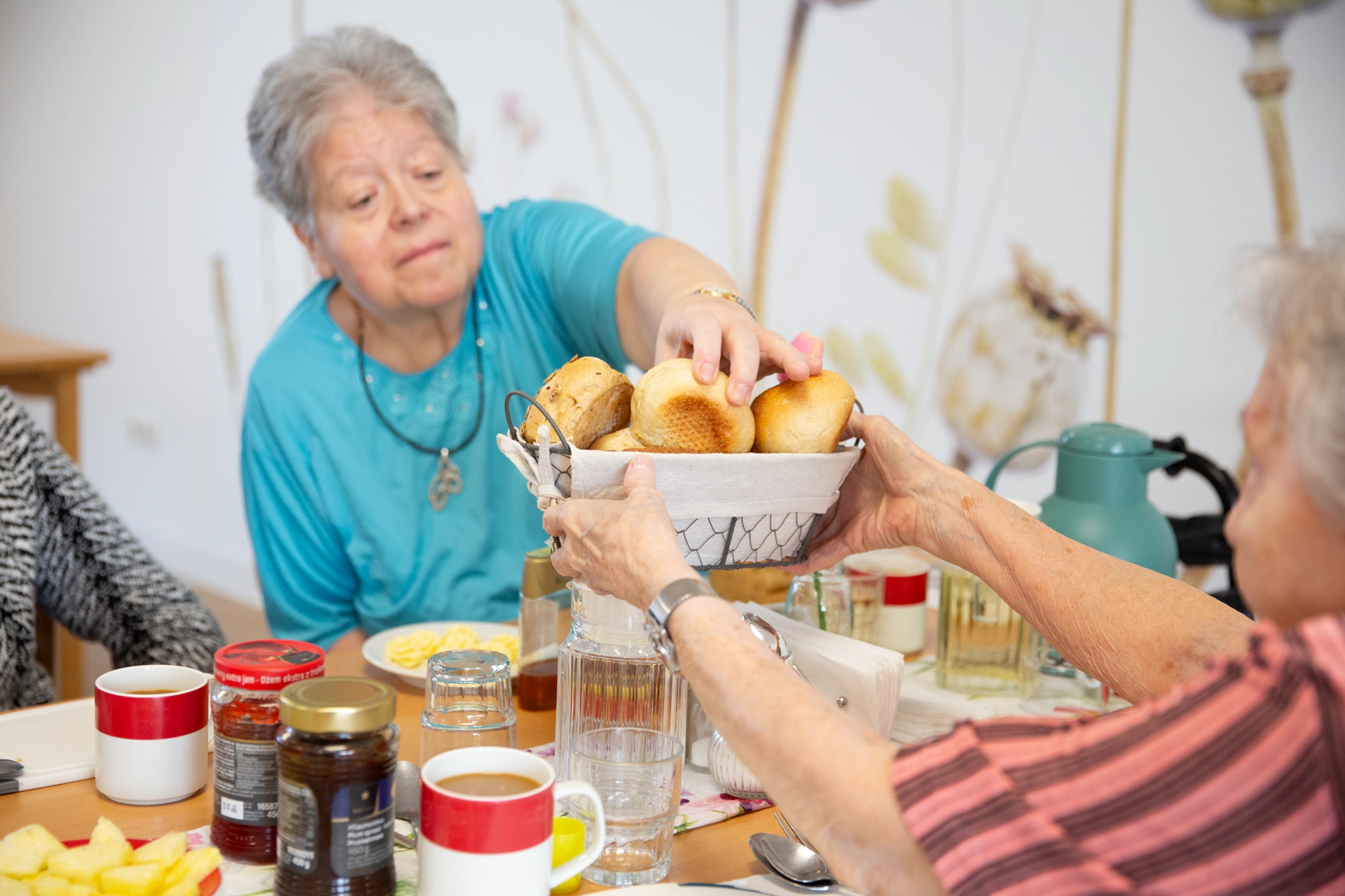Seniorin greift beim gemeinsamen Frühstück im Pflegeheim Am Hofwiesenpark nach einem Brötchen.