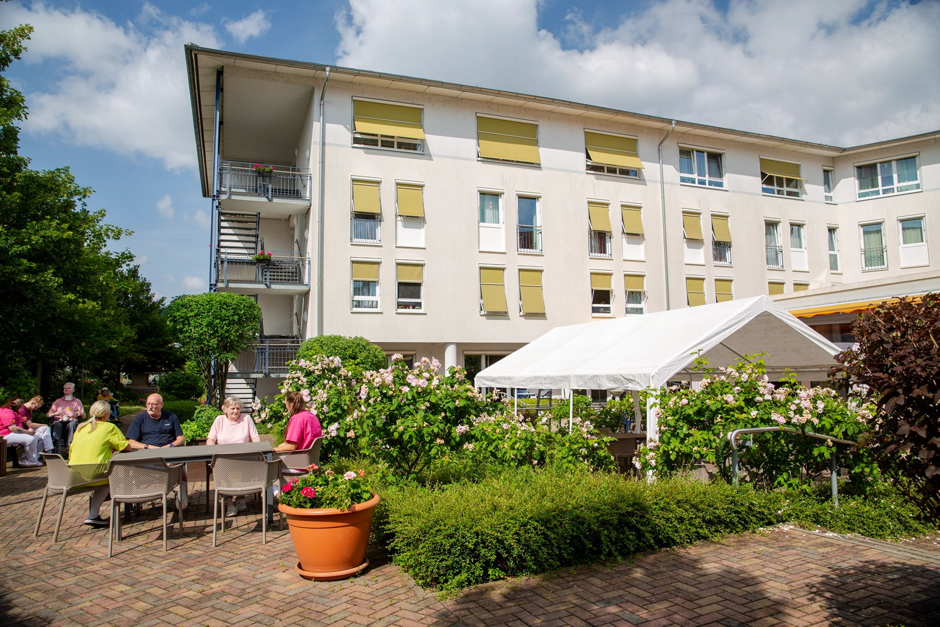 Bewohnerinnen und Bewohner genießen bei Sonnenschein die blühende Gartenanlage des Pflegeheims Am Hofwiesenpark.