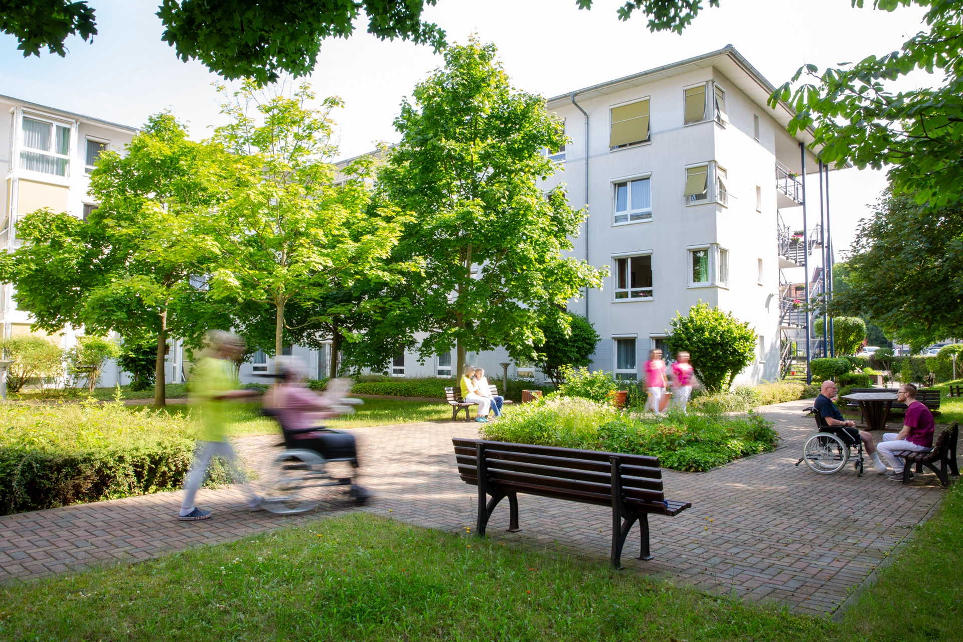 Bewohner und Pflegekräfte bewegen sich im begrünten Innenhof des Pflegeheims Am Hofwiesenpark in Gera.