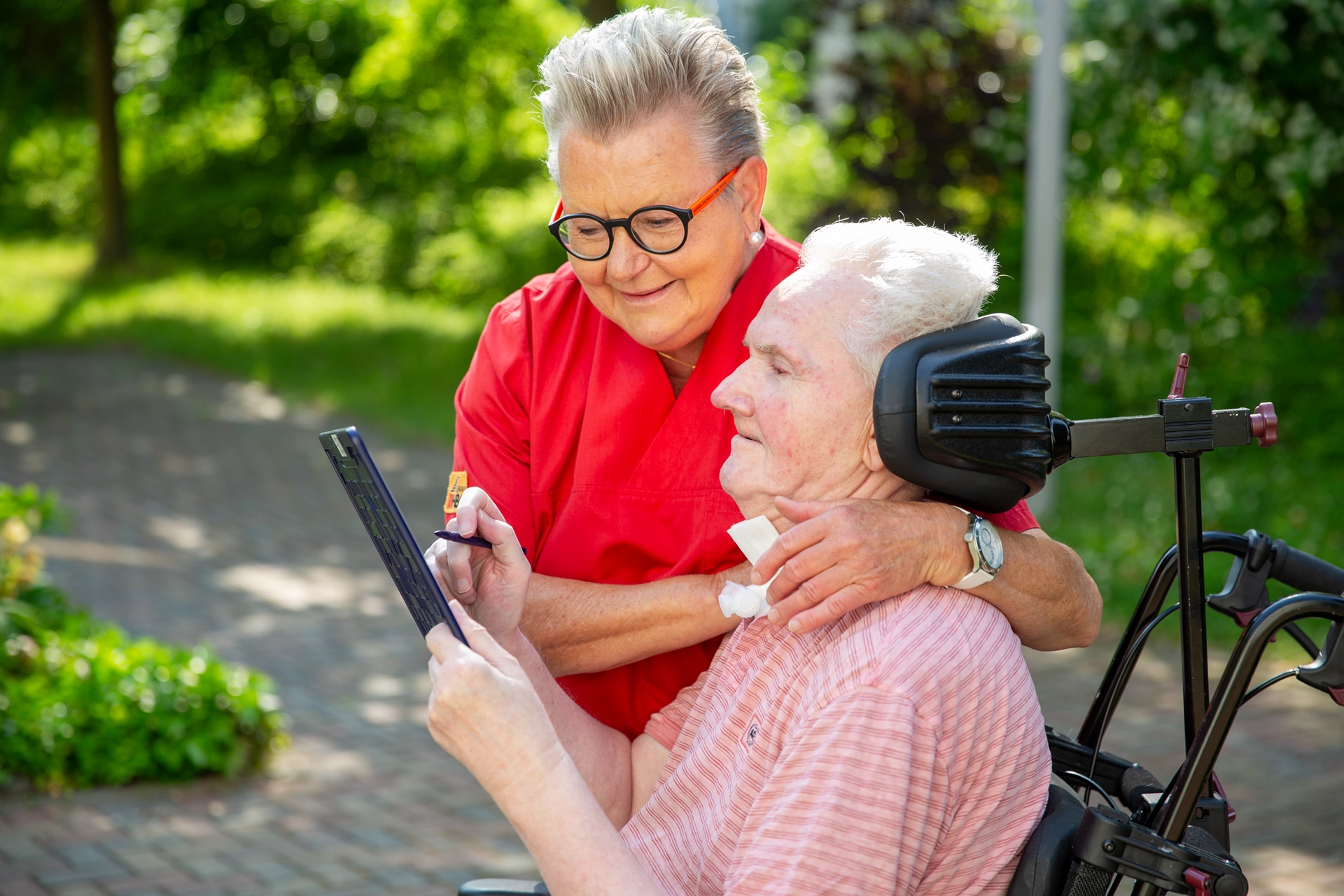 Pflegekraft zeigt einem Bewohner im Rollstuhl ein Tablet im Garten des Pflegeheims Am Hofwiesenpark.