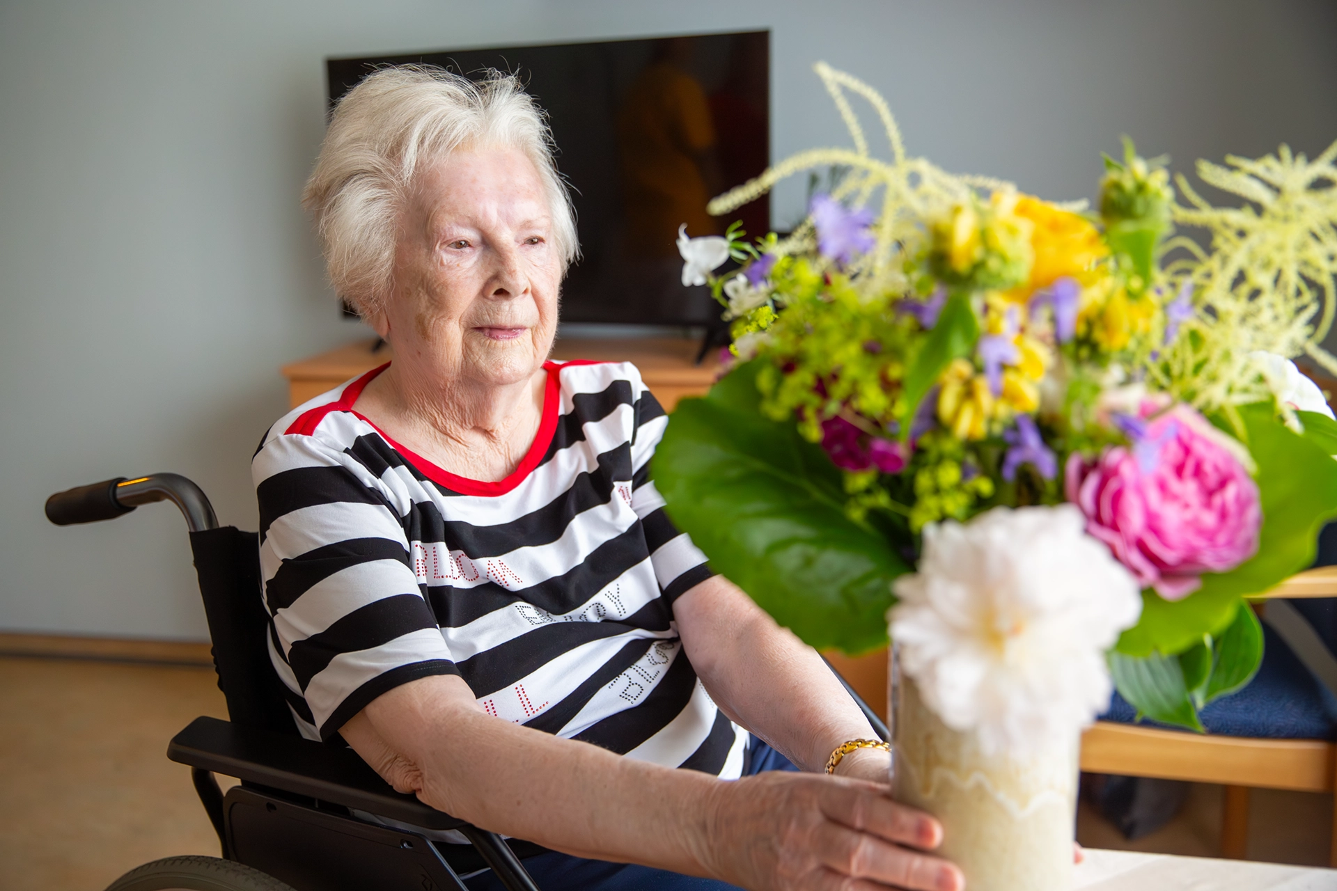 Seniorin im Rollstuhl betrachtet einen bunten Blumenstrauß.