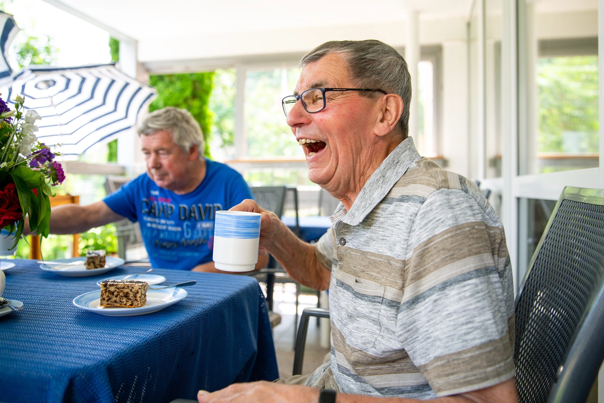 Zwei Senioren bei Kaffee und Kuchen, einer davon lacht herzlich
