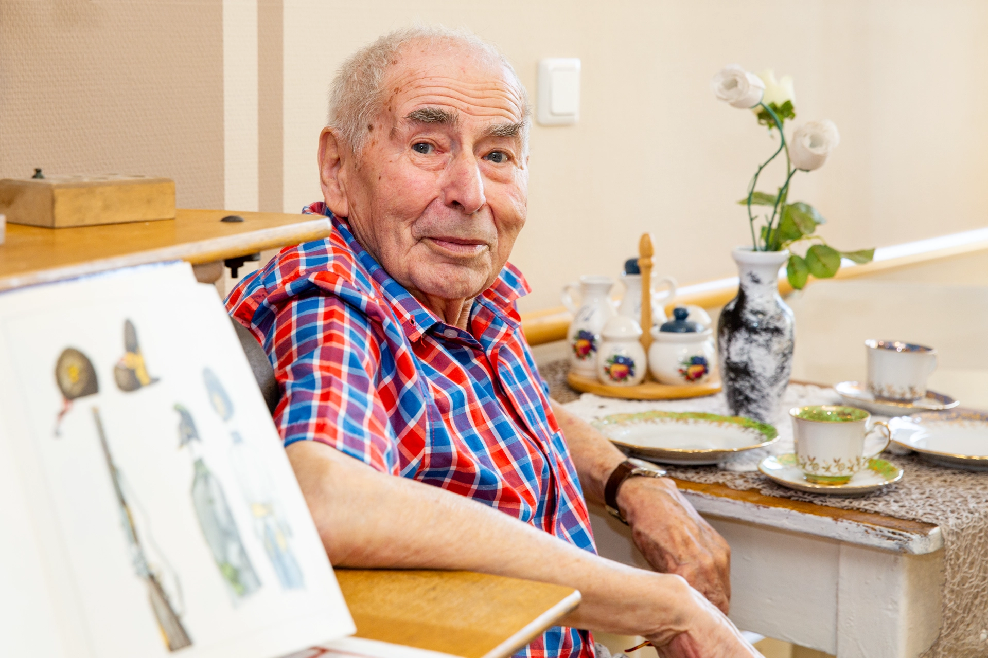 Senior sitzt mit Kaffeegeschirr im liebevoll eingerichteten Stübchen.