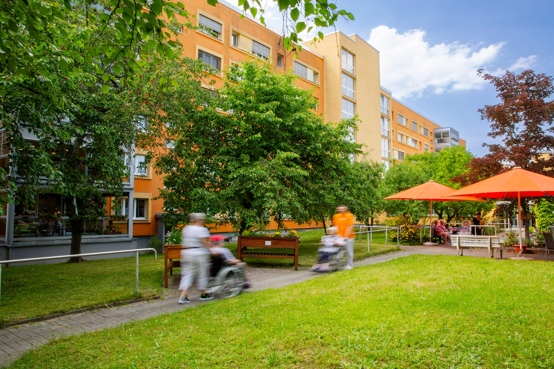 Gartenansicht mit Sitzgruppen, Sonnenschirmen und dem Pflegeheim im Hintergru