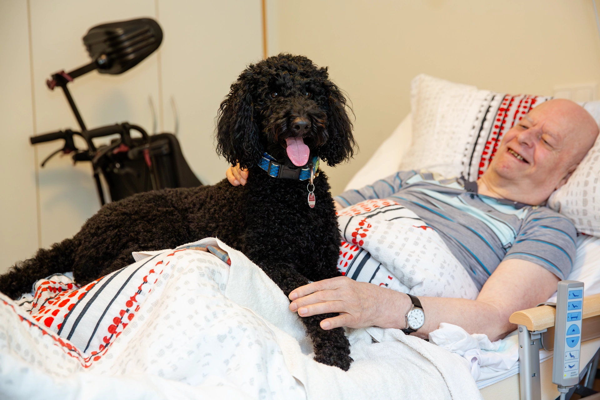 Ein lachender Bewohner liegt im Bett, während ein schwarzer Hund neben ihm sitzt