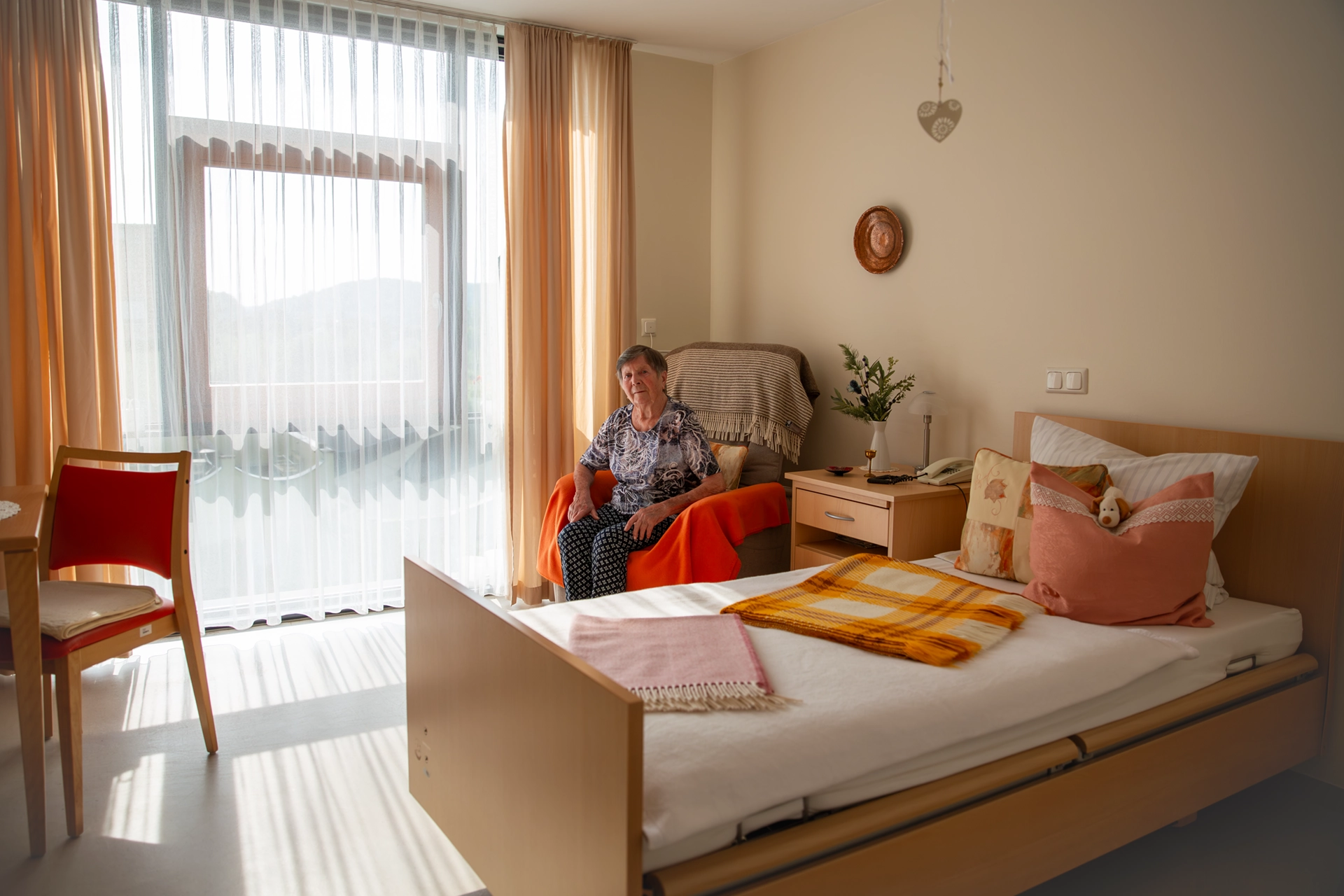 Seniorin sitzt im gemütlich eingerichteten Einzelzimmer mit großer Fensterfront im Pflegeheim Otto Dix der HBG Gera