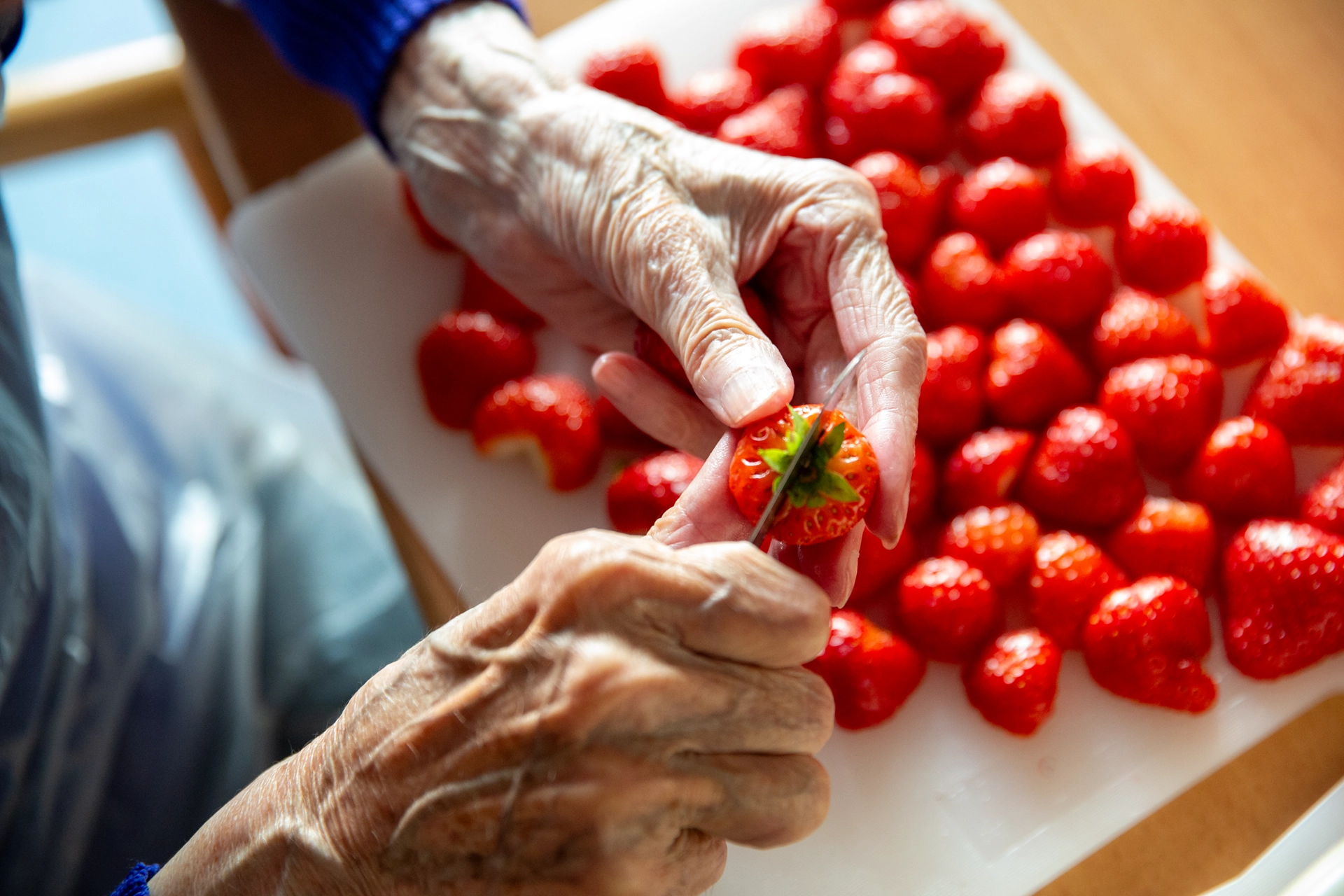 Eine Seniorin schneidet frische Erdbeeren auf einem Schneidebrett.