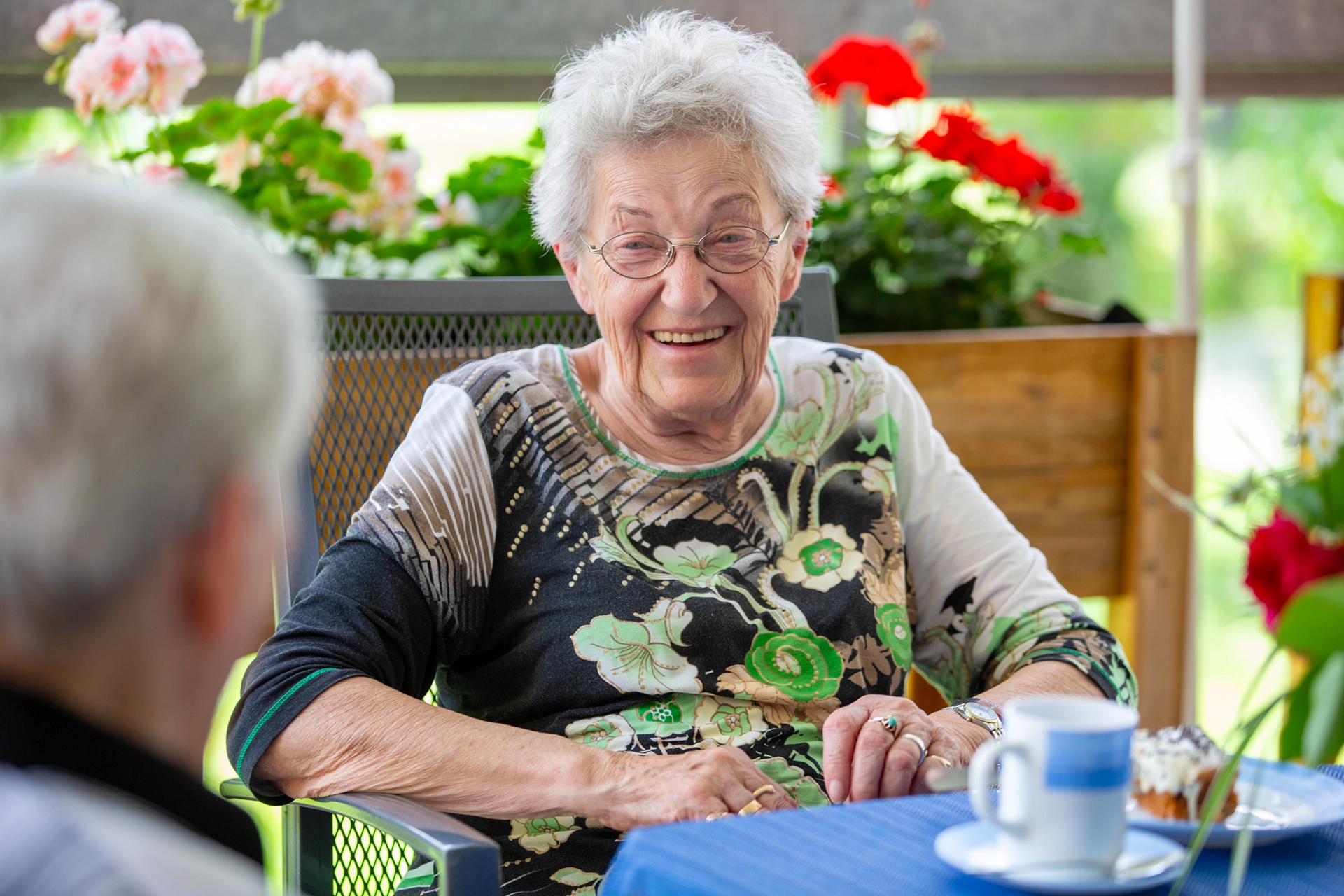 Lachende Seniorin im Gespräch mit einer anderen Person in einer Tagespflegeeinrichtung der HBG Gera